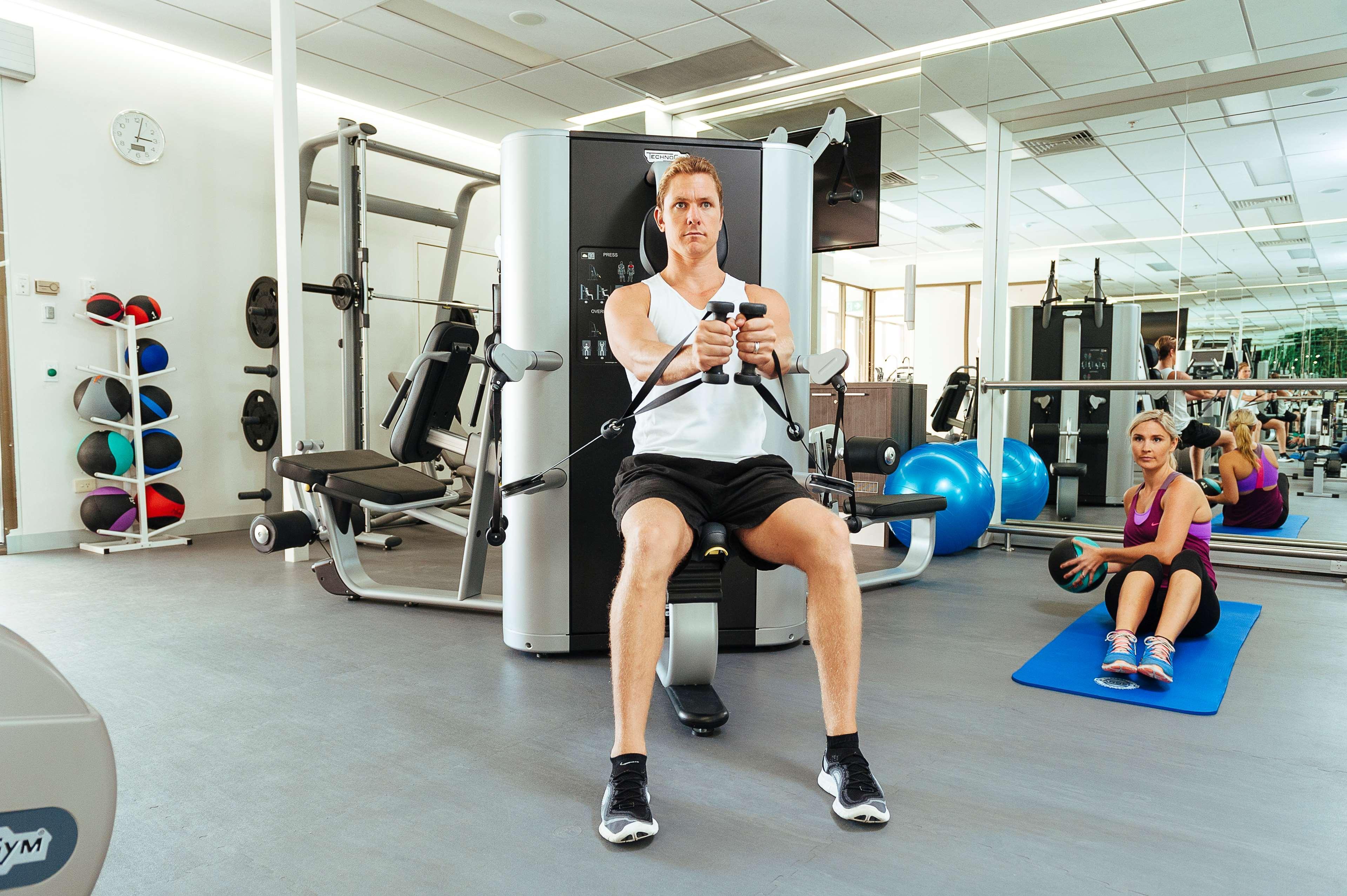 Отель Stamford Plaza Аделаида Экстерьер фото The photo shows a gym setting with two individuals engaged in workout activities. 

In the foreground, a man is seated on a machine, using the handles to perform a rowing exercise. He is wearing a sleeveless shirt and shorts, indicating an active wor
