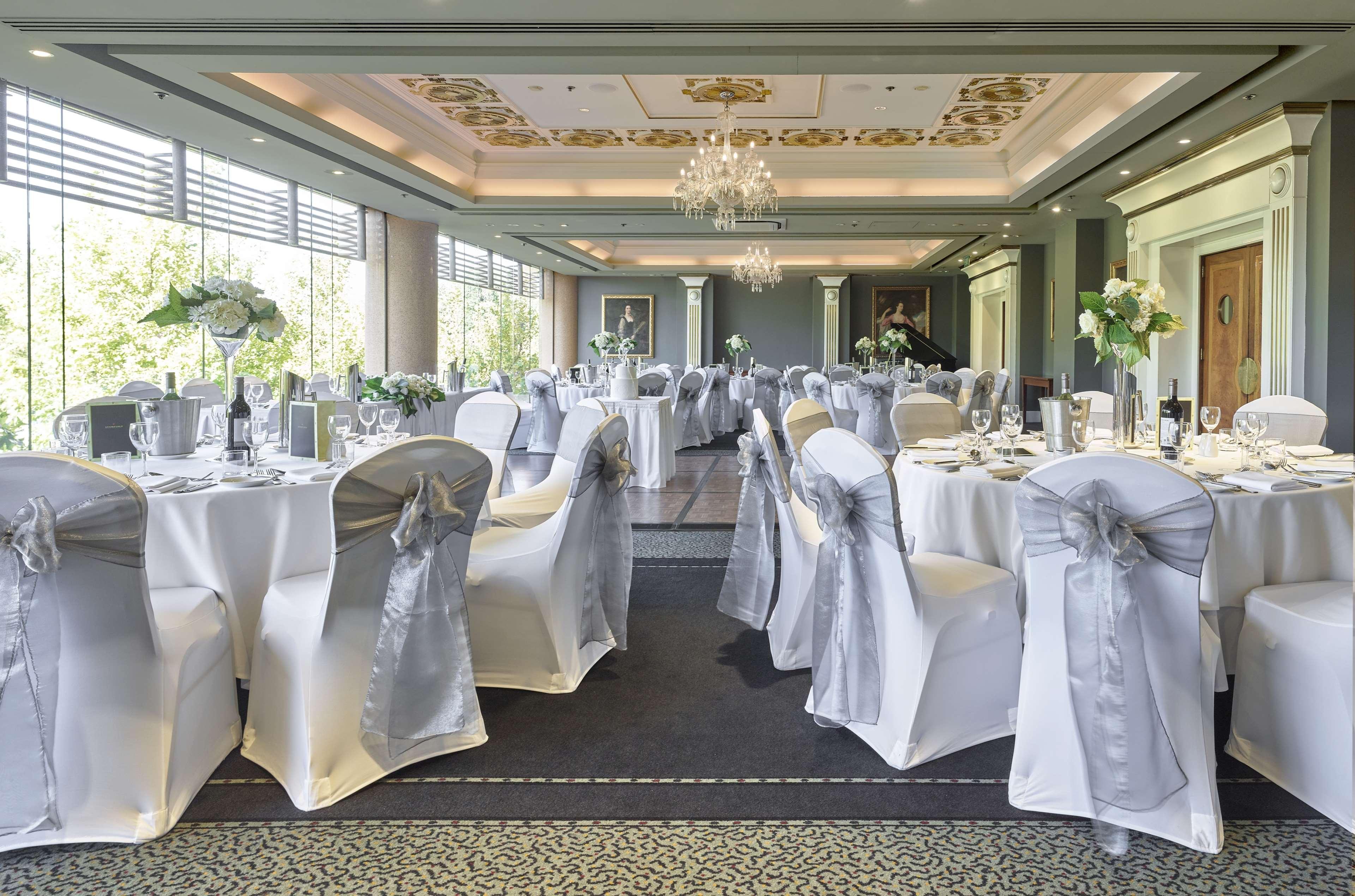 Отель Stamford Plaza Аделаида Экстерьер фото The photo displays an elegantly arranged banquet hall. The room features several round tables covered with white tablecloths, each adorned with silver sashes on the chairs. There are floral centerpieces, possibly white flowers, on the tables, adding 