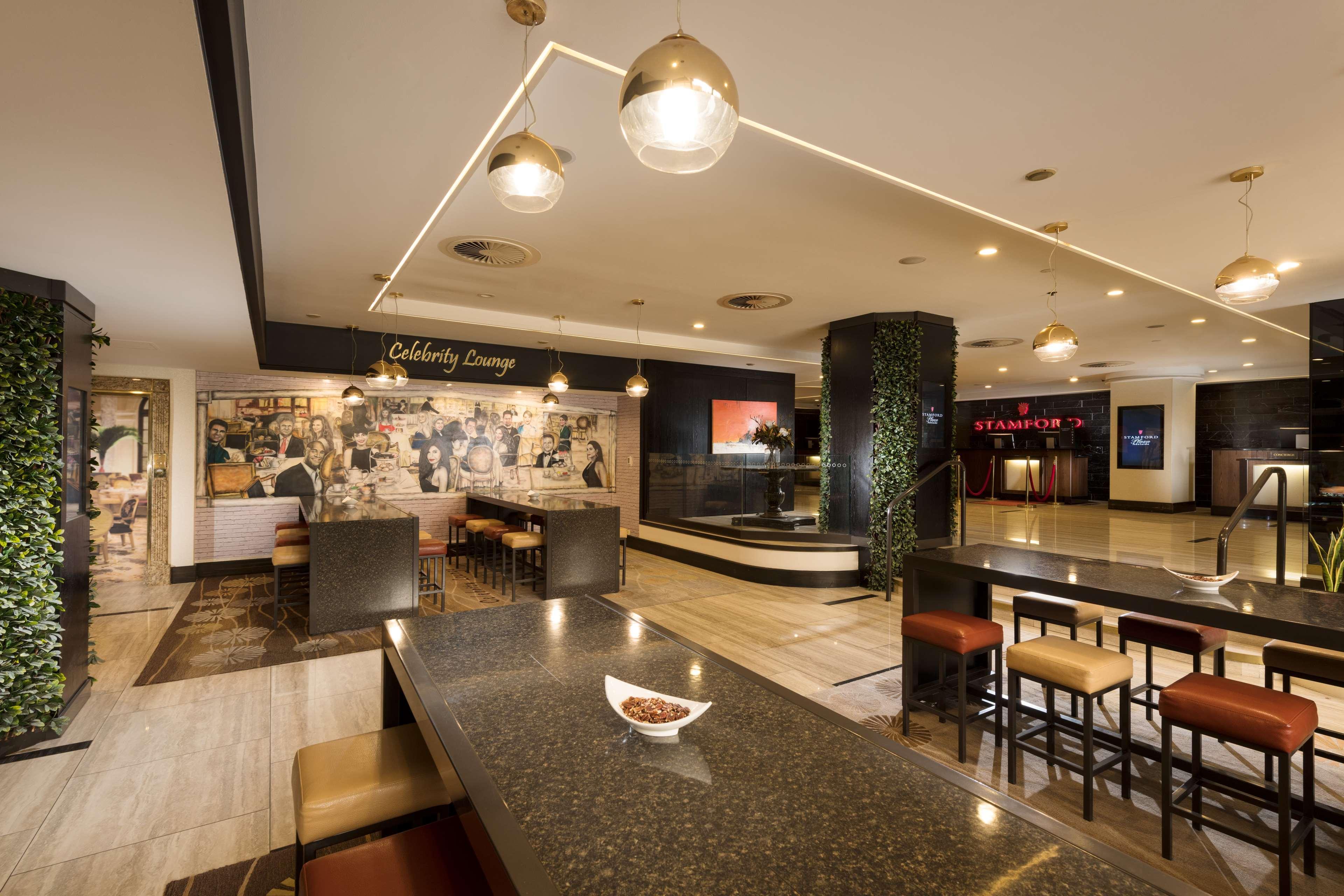 Отель Stamford Plaza Аделаида Экстерьер фото The photo shows a modern and stylish interior of a lounge or restaurant area. Prominent features include a long dark countertop with bar stools, and several pendant lights hanging from the ceiling. In the background, there is a mural or artwork that 